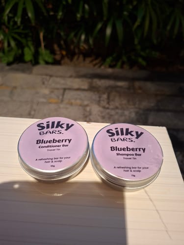 Customer's Blueberry shampoo and conditioner bars in round metal tins, sitting on a table.