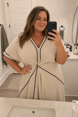 Customer's beige V-neck midi dress with black piping and knot detail worn in a bathroom