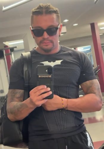 Reviewer in a mirror selfie wearing a fitted black Batman compression tee with a structured emblem design at the gym.