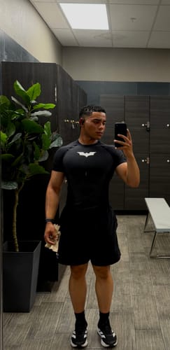 Customer's Batman compression tee in black, worn during a workout in a gym locker room.