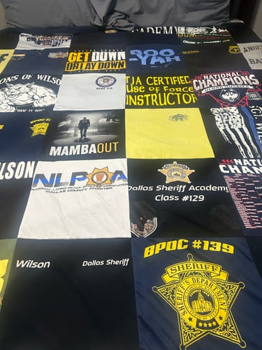 Customer's Project Repat T-Shirt Quilt featuring various custom graphic logos and text squares on a bed.