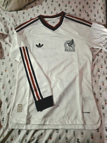Customer's white Mexico Visita 2026 jersey with black and red accents, laid out on a patterned surface.