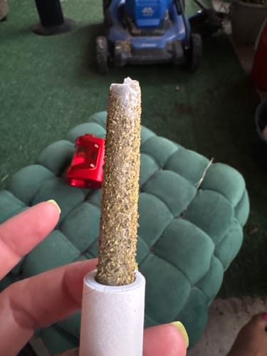 Customer's hand holding a Summit pre-roll, which is covered in golden kief and features a white glass tip.