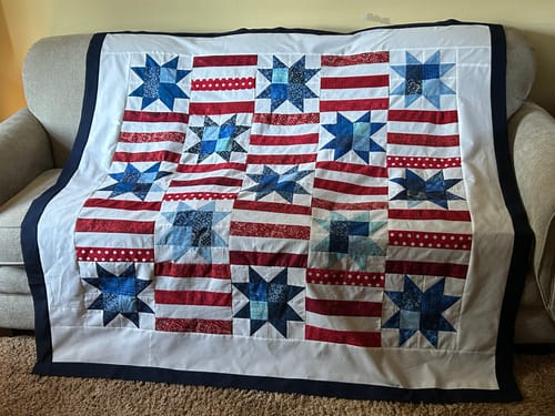 Customer's Red, White, and Cute quilt draped over a sofa, featuring patriotic red, white, and blue star-patterned blocks.