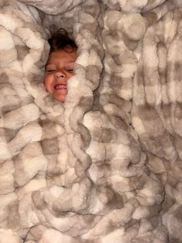 Customer's child bundled in the plush, cream gingham Hugs Sophia Blanket.
