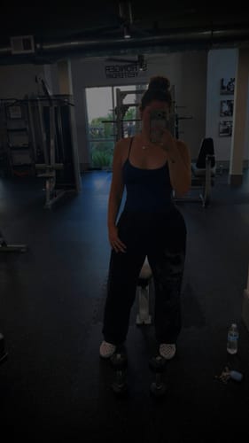 Reviewer in a gym wearing Divine Sweatpants with a skull graphic, standing in a fitness center.