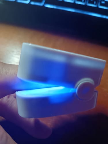 Customer's white Onychom laser device for nail treatment in use on a finger with a bright blue light.