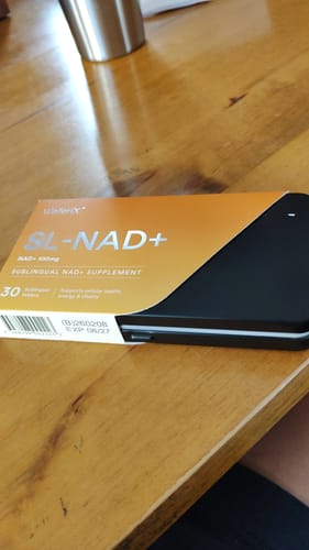 レビューアが木製テーブルの上に置いたSL-NAD⁺サプリメントの黒とオレンジのパッケージ。