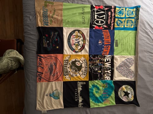 Customer's Project Repat T-Shirt Quilt featuring various colorful printed squares laid flat on a striped bedspread.