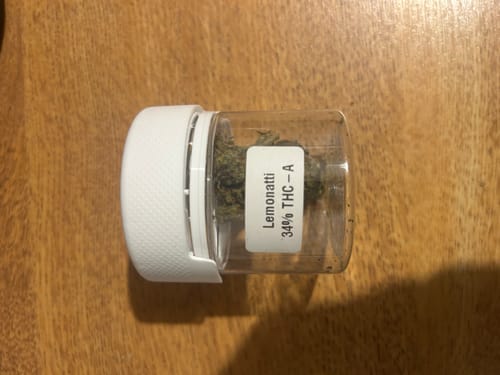 Customer's Lemonatti THC-A flower inside a clear plastic container with a white cap sitting on a wooden surface.