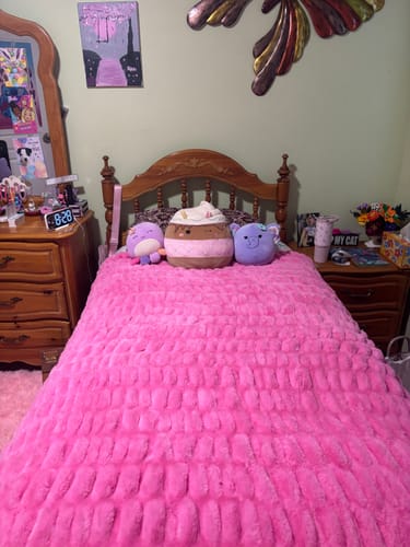 Customer's plush pink Hugs blanket spread over a bed with decorative plush toys.