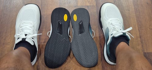 Customer's two pairs of CUURT Muuv court shoes on a wooden floor, showing white uppers and black treaded soles.