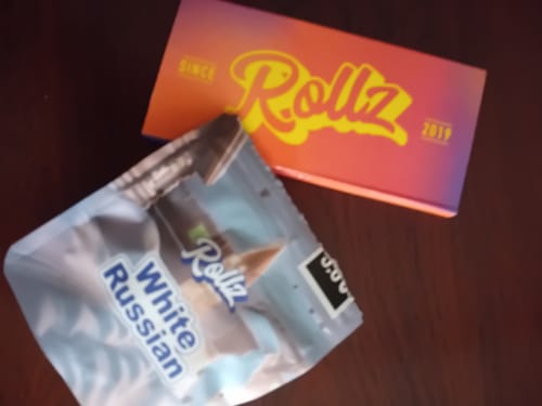 Customer's White Russian THCA flower bag next to a colorful Rollz branded product box on a table.