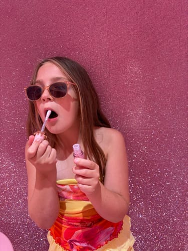 Customer's person applying shiny lip gloss from the Walk Ins collection in front of a sparkling pink wall.