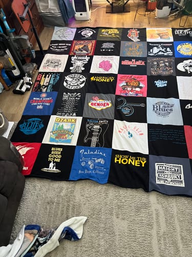 Customer's Project Repat T-Shirt Quilt laid out on a carpeted floor showing a patchwork design of various graphic shirts.