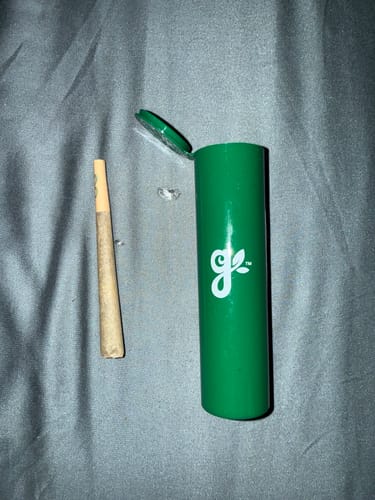 Customer's Royal Cherry Pre-Roll with tan filter resting beside its open green storage tube.