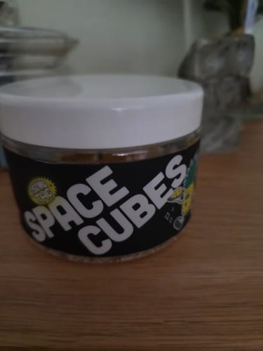 Kundenfoto des THC Space Cubes Behälters mit schwarzem Etikett auf einer Holzoberfläche.