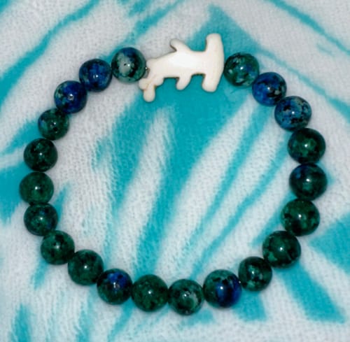 Customer's Shark Week Bracelet with blue-green beads and a hammerhead charm on a tie-dye fabric surface.