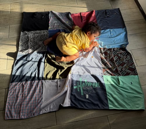 Customer's Project Repat T-Shirt Quilt featuring colorful squares with a child cuddling on top on a wooden floor.