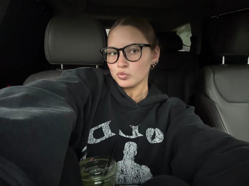 Reviewer's black Gold's Gym Classic Pullover hoodie being worn for an oversized fit while sitting in a car.