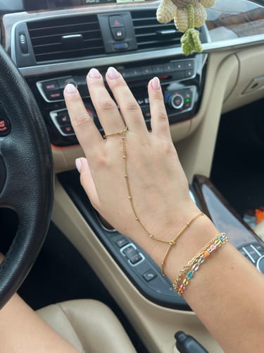 Customer's gold hand chain bracelet with delicate beads worn on hand, seen inside a car.