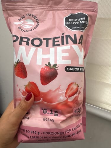 Customer's hand holding a bag of Proteína Whey fresa, featuring strawberry illustrations and clear branding.