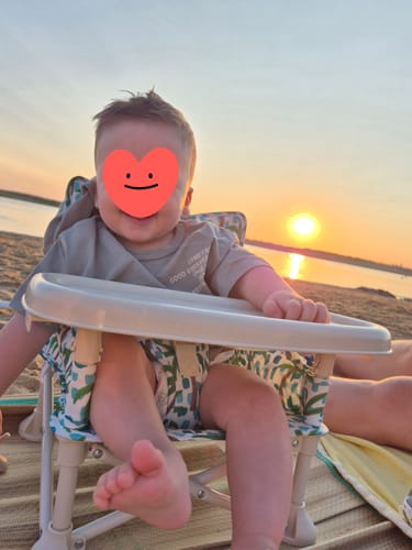 Customer's Kai baby chair on a beach at sunset, with a child seated and smiling.