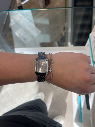 Customer's silver Claire De Mains watch with a mesh band worn on a wrist alongside a thin gold-toned bracelet.