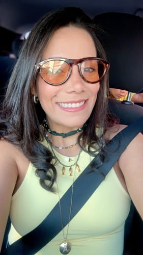Customer's Óculos de Sol Iracema com lentes claras e armação escura, vestindo o modelo no rosto dentro de um carro.