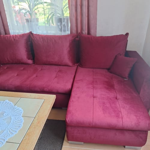 Kliento LOKO minkštas kampas tamsiai raudonos spalvos, pastatytas svetainėje prie lango.