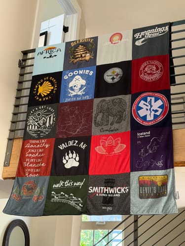 Customer's Project Repat T-Shirt Quilt hanging over a loft railing, featuring various colorful fabric squares.