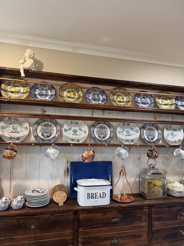 Customer's Maxime French Provincial Cherub Figurine sitting on the top shelf of a large wooden plate rack display.
