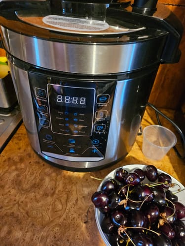 Recenzent arătând multicookerul Novio SteelCook pe un blat de bucătărie, cu panoul digital aprins.