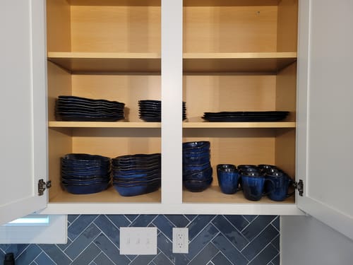 Customer's Ocean Blue Organic Oval Plate Set neatly stacked on shelves inside a kitchen cabinet.