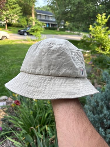 A customer holds up their light-colored Big Standard Bucket Hat outdoors.