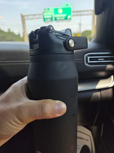 Customer holding their black Bottle Buddy with its new replacement lid inside a car.