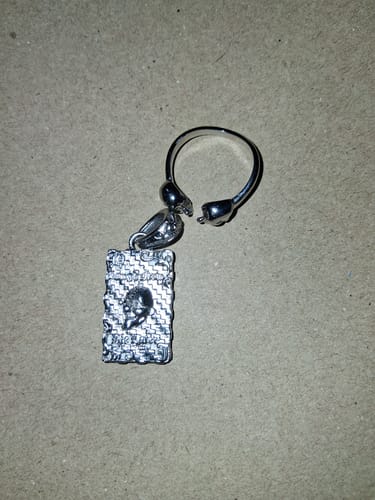 Reviewer's silver Laugh Now Cry Later Ring and bonus pendant lying on a textured surface.