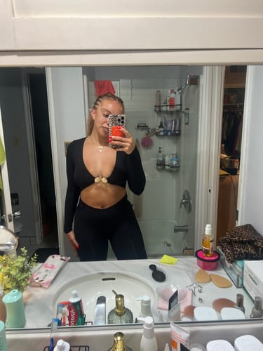 Reviewer takes a mirror selfie wearing the black Naked Cutout Capri Jumpsuit, showing the front cutout and gold hardware.