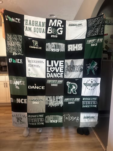 Customer holding up a large T-Shirt Quilt made from dance team shirts in black, green, and white.
