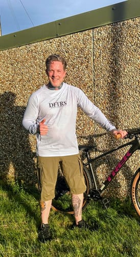 Reviewer wearing a white long-sleeve Flowteq™ Jersey, standing with his mountain bike outdoors.