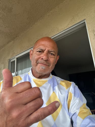 Reviewer outdoors wearing a golf polo with a yellow and purple diamond pattern, making a hand gesture.