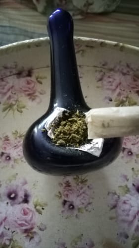 Reviewer emptying a Cherry Dosi Do Pre-Roll into the bowl of a dark glass pipe.