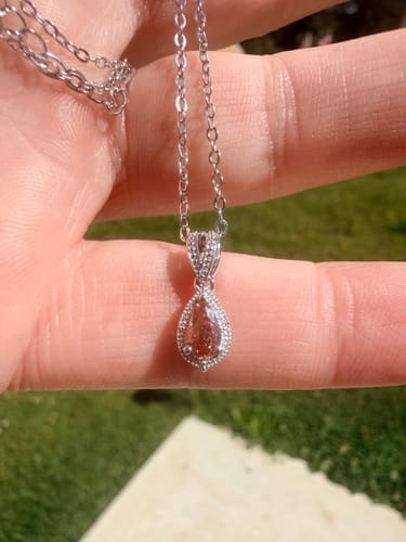 Reviewer holding the DovEggs pear diamond pendant necklace across their fingers in the sunlight.