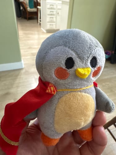 Customer holding their Finch Plush Bag Charm, which is wearing a small, red Supergirl cape.