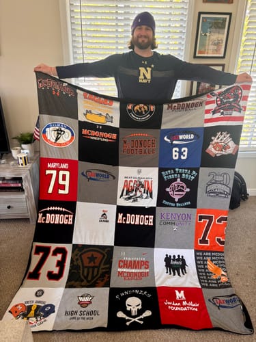 Customer holding up a large Project Repat T-Shirt Quilt made from many different sports and school t-shirts.