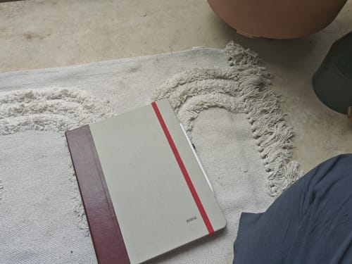 Customer's custom book-style iPad case in grey with a burgundy spine and red elastic band, resting on a rug.