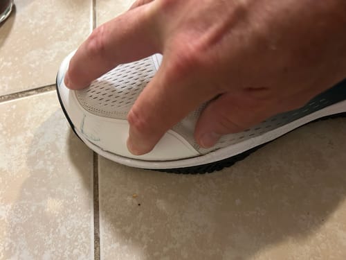 Close-up of a reviewer's hand pressing on the area where the sole has separated from the white CUURT Muuv shoe.