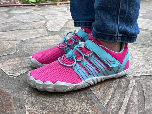 Rezensent zeigt eine Seitenansicht seiner pinken und hellblauen Vigor II Barfußschuhe.