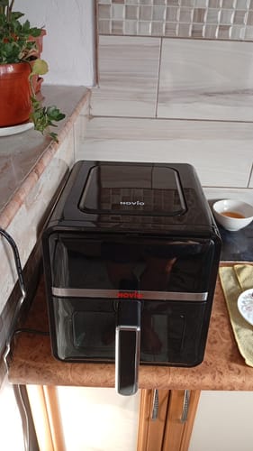 Client arătând friteuza Air Fryer Novio StonePro neagră, așezată pe blatul de bucătărie.