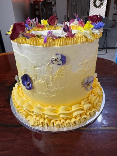 Customer's tall yellow cake decorated with colorful VIOLAS edible flowers on the top and sides.